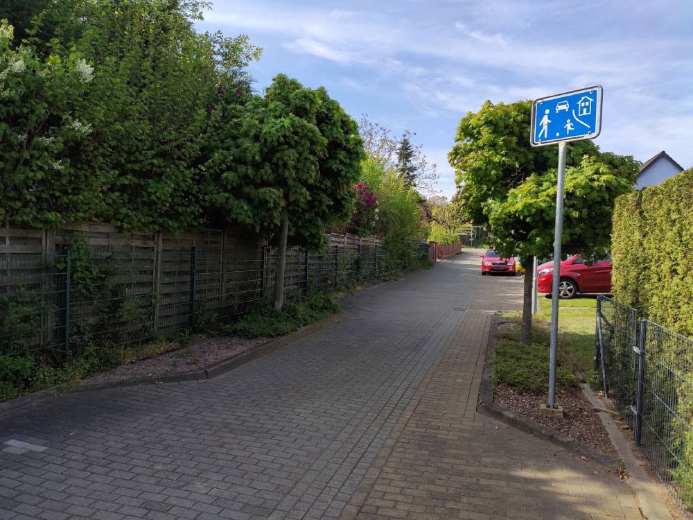Verkehrsberuhigter Bereich in Haldensleben mit gepflanzten Bäumen beidseitig und blauem Verkehrsschild für Spielstraße am Straßenrand.